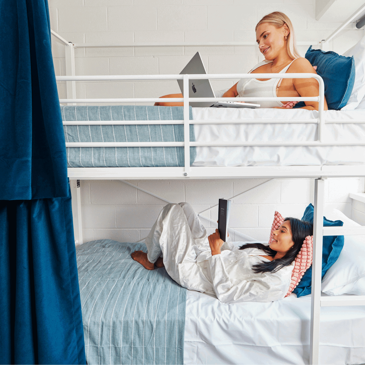 Two travellers lying on bunk beds, both reading on phone or book