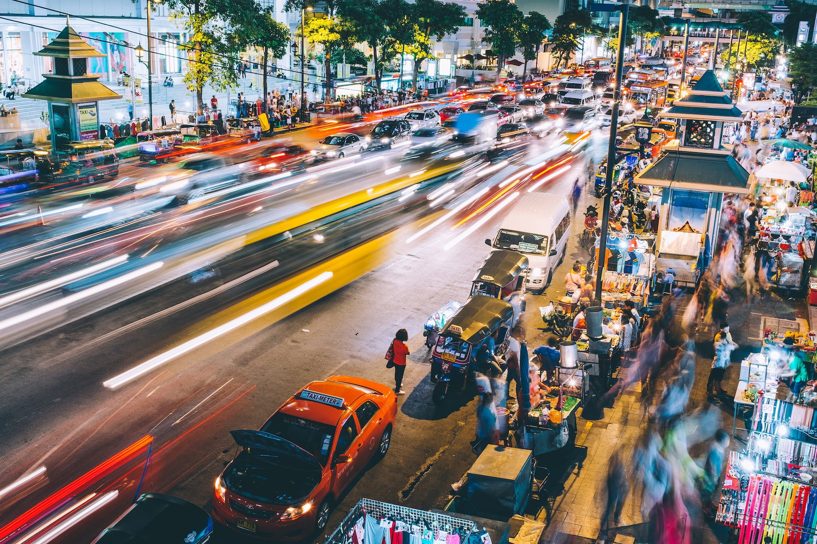 Timelapse photo of a busy Bangkok street lined with Tuk Tuks and market stalls