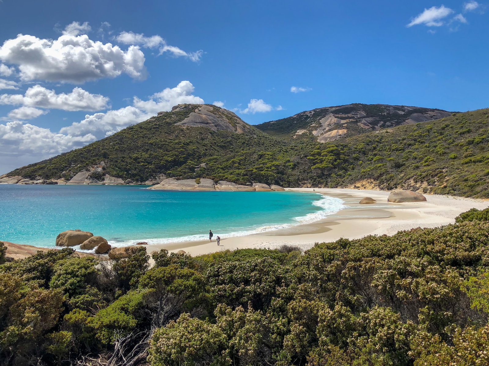 A pristine beach with blue water surrounded bu lush greenery and mountains
