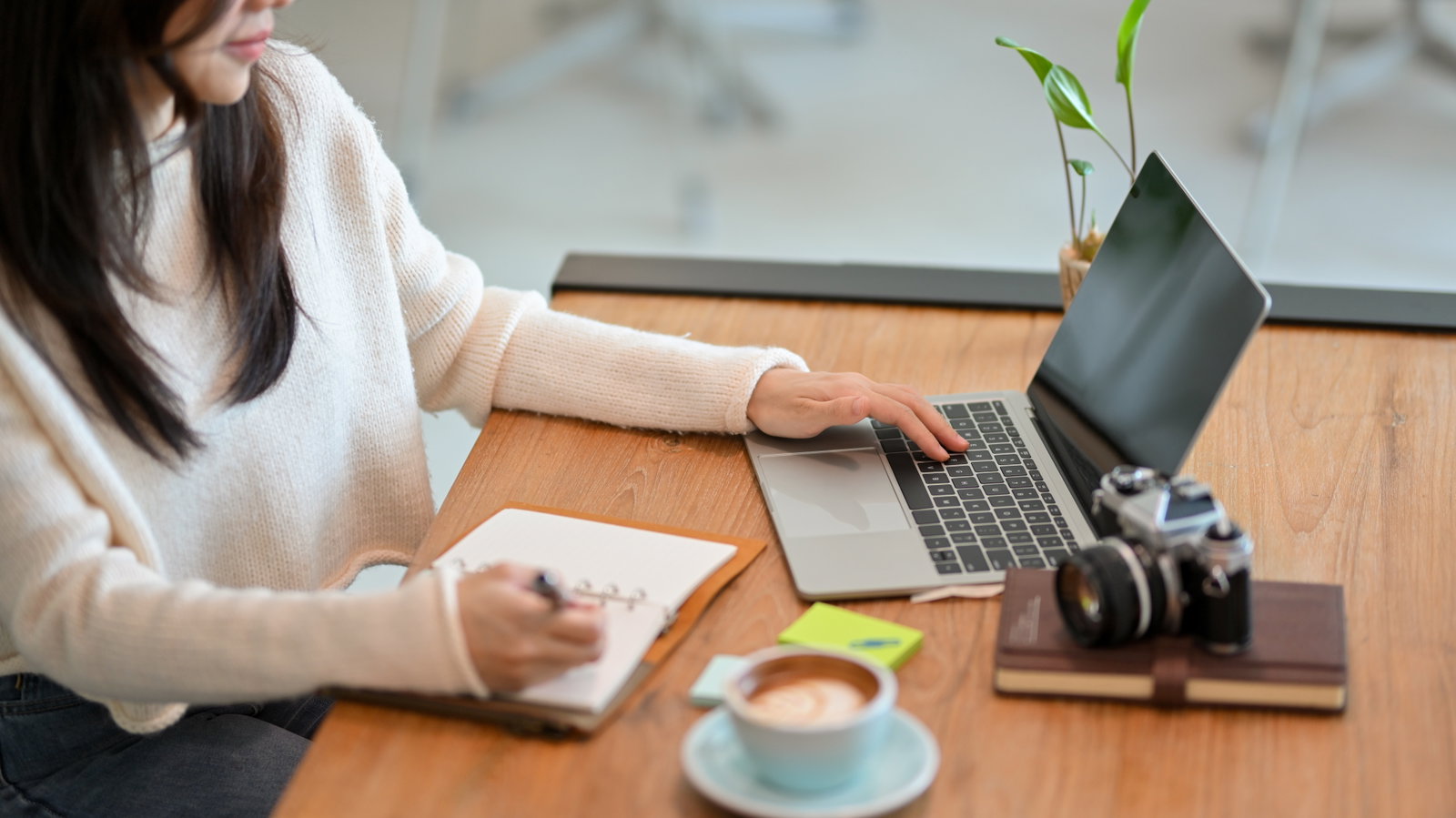 Person writing in note book and using laptop