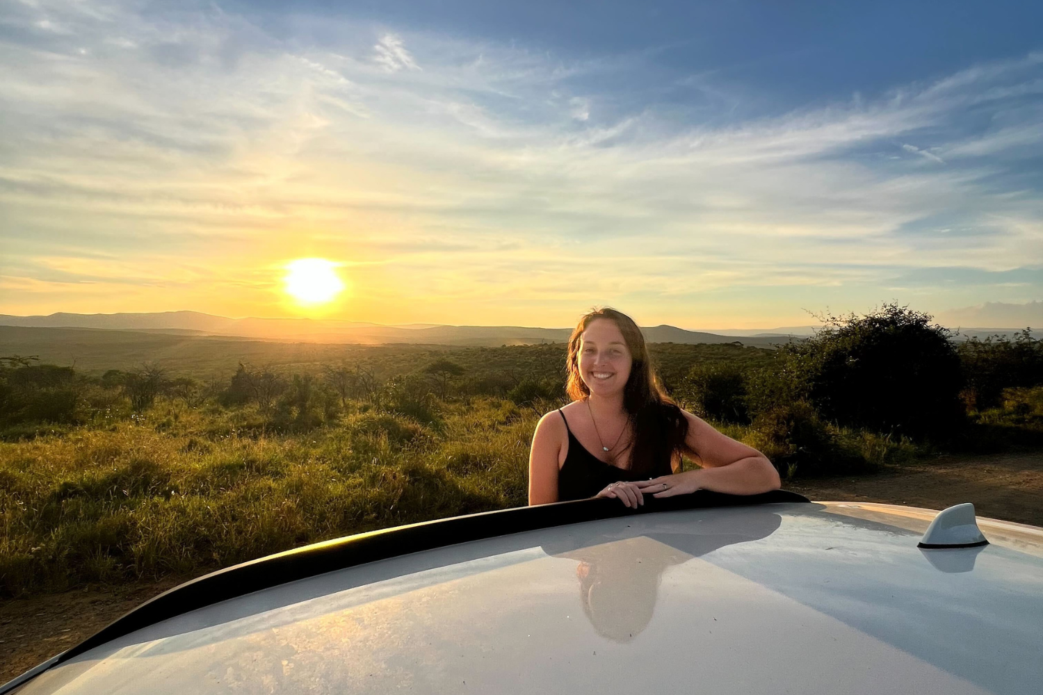 Traveller stood on side of safari jeep with sunset behind in South Africa