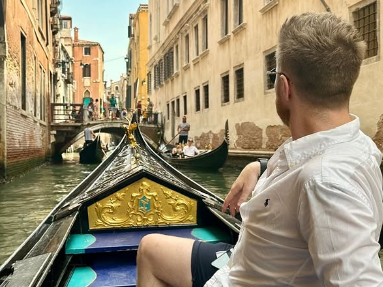 Traveller sat on gondola down canal in Venice