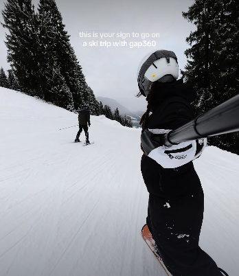 Traveller holding a camera behind them as they snowboard down the mountains in the Austrian Alps on a group trip