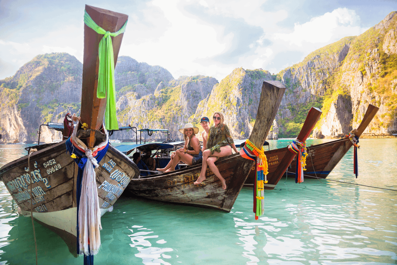 Group of travellers sat on long boats in thailand maya bay