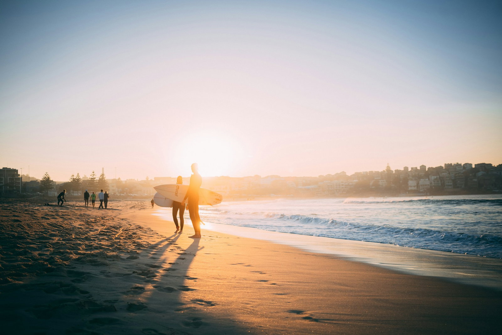Two surfers hanging out on the beach with their boards, sunset, crashing waves and golden sand, group in the distance